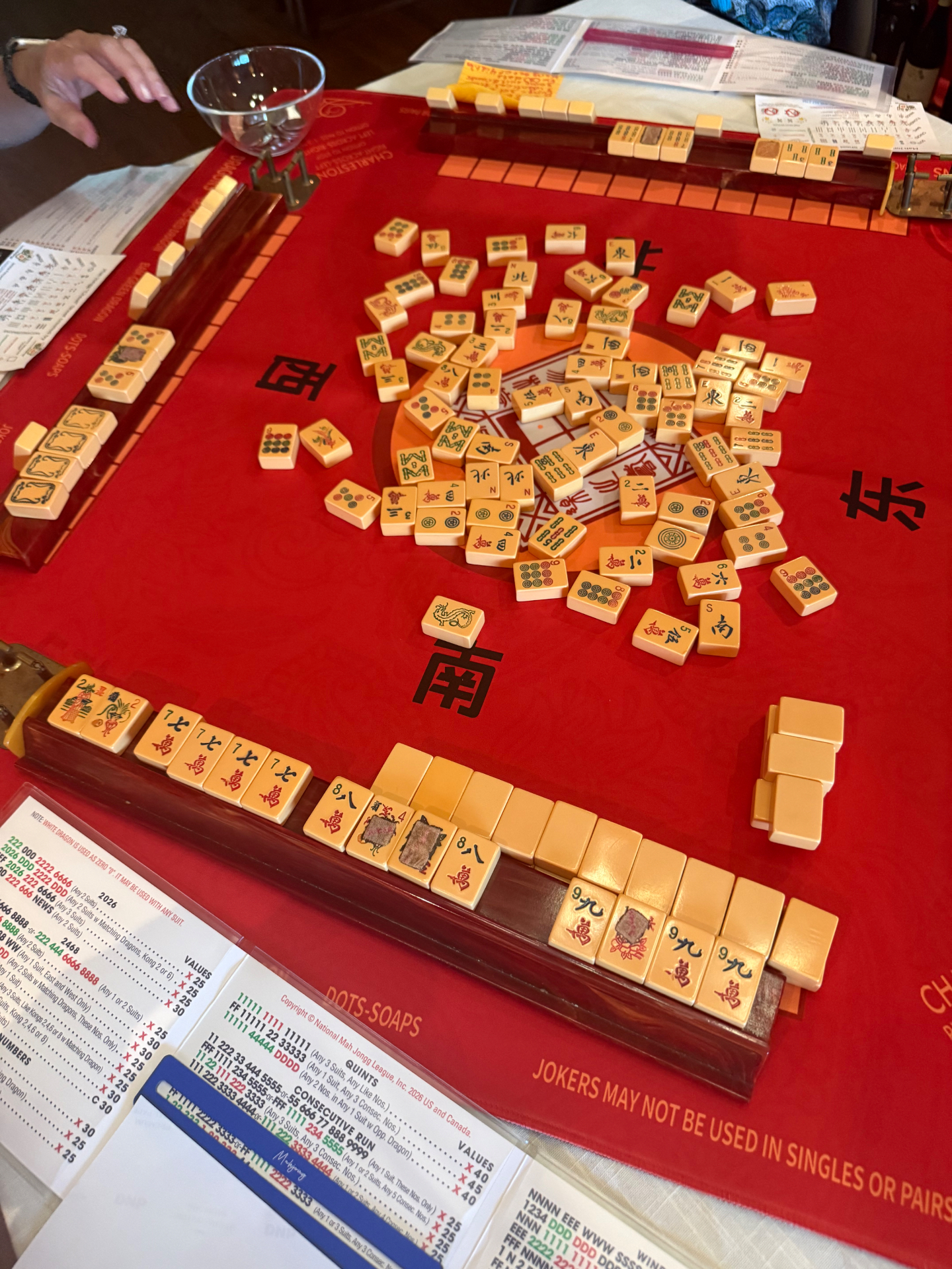 A live game in progress: racks, tiles and the official card on a red MahJongg mat